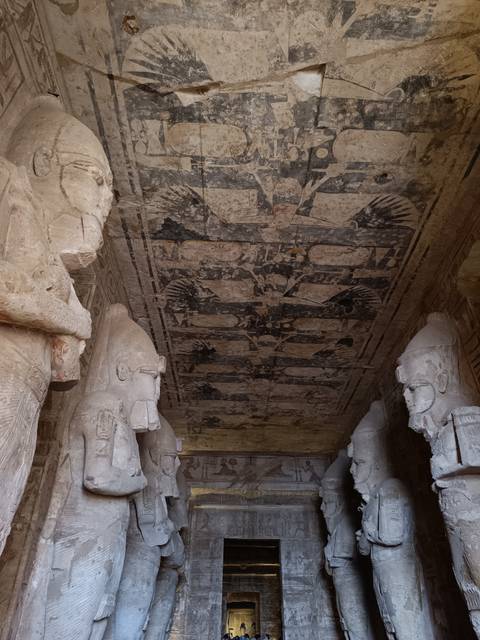 Interior ceiling of ancient Egyptian temple with faded bird motifs between two colossal heads.