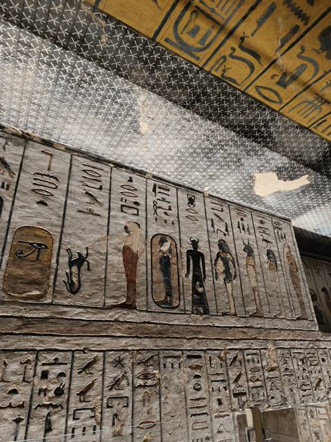 Close-up view of ancient Egyptian hieroglyphs and painted deities on a tomb ceiling and wall.
