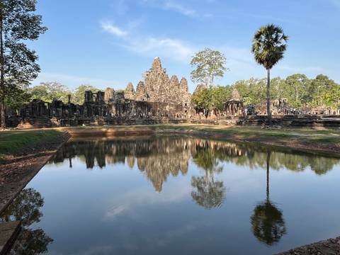 Ancient Bayon temple towers reflected perfectly in a still pond under clear blue sky.