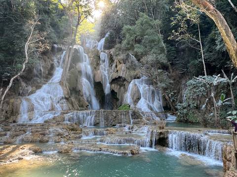 Multi-tiered Kuang Si waterfall cascades through limestone pools surrounded by dense green jungle.
