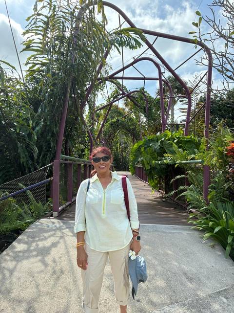 Woman standing on elevated wooden walkway surrounded by dense tropical foliage in a garden park.