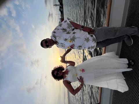 Couple playfully framing the setting sun aboard a boat against colorful sky and calm sea.
