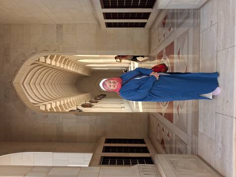 Smiling woman in headscarf poses in arched marble corridor of a grand mosque.