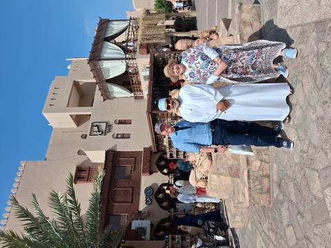 Tourists stand with a local vendor outside a bustling market of pottery and crafts.