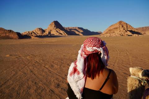 Back view of traveller wearing keffiyeh looking over vast desert landscape and rugged sandstone peaks.