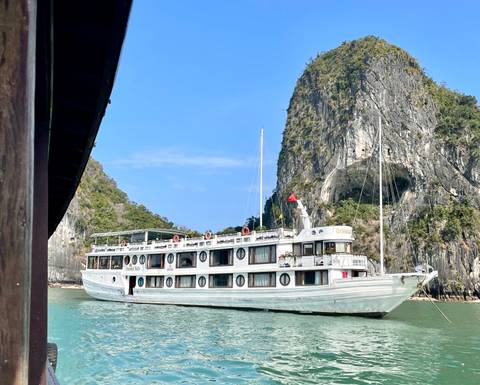 White overnight cruise ship sailing between towering limestone cliffs in emerald waters