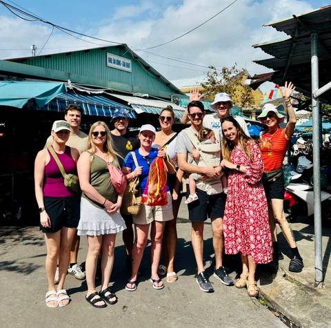 Happy travel group posing at an outdoor Vietnamese market under bright sunlight
