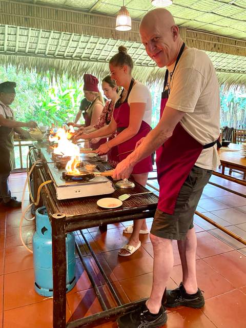 Participants in aprons flambé dishes during an interactive Vietnamese cooking class