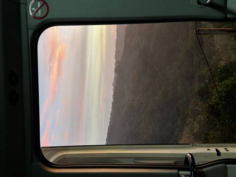 View through a vehicle window of forested hills at dawn with pastel sky hues.