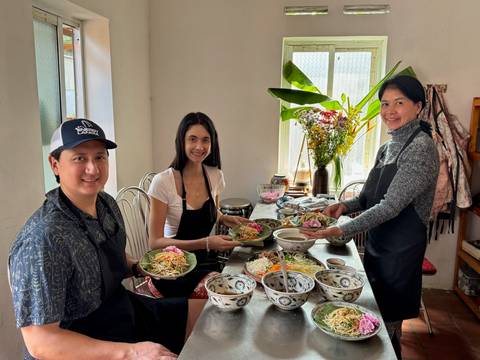 Small cooking class holding plates of prepared Vietnamese dishes in a bright kitchen.