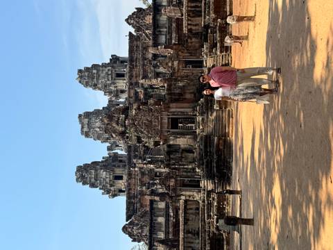 Couple posing in front of an ancient Angkor temple under blue sky.