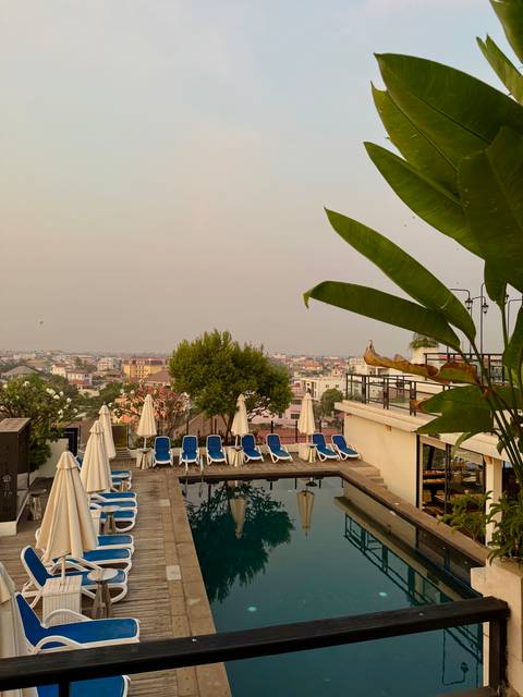 Rooftop hotel pool with sun-loungers overlooking a hazy Vietnamese town.