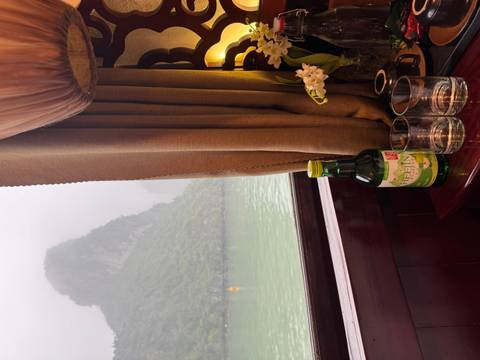 Wine bottle and glasses on a cruise cabin windowsill overlooking limestone peaks and green water.