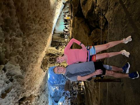 Two travellers pose inside a vast limestone cave illuminated by artificial lights.