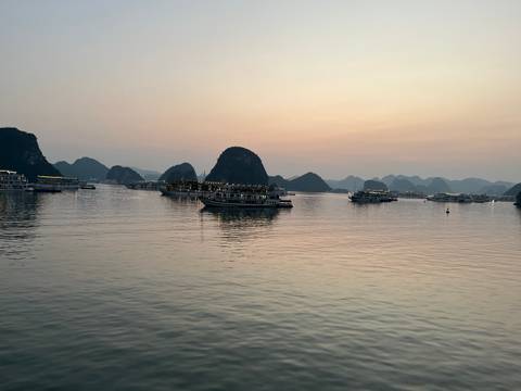 Serene sunset over jade waters dotted with cruise boats and limestone karsts.