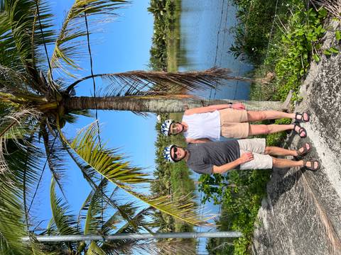 Couple in bike helmets stand by a lagoon and palm trees on a sunny day.