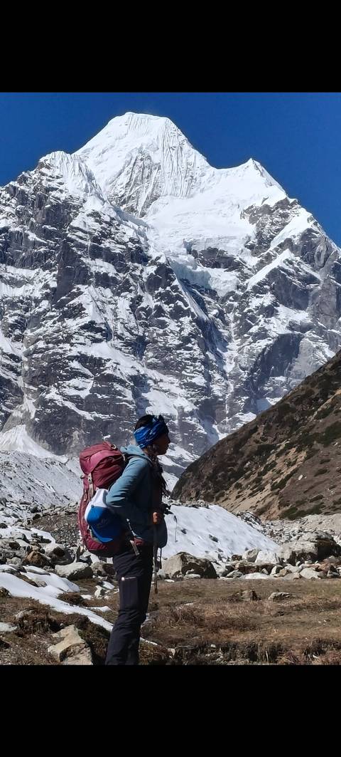 Solo trekker with backpack pauses before immense snow-covered Himalayan walls.