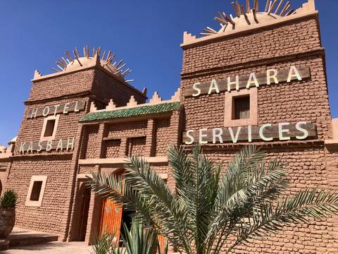 Clay-brick facade of Sahara Services Hotel Kasbah with decorative roof and palm fronds.