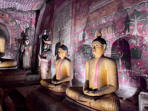 Row of brightly painted Buddha statues and murals inside Dambulla Cave Temple lit dramatically.