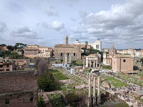 Panoramic overlook of the Roman Forum ruins framed by historic buildings and cloudy skies.