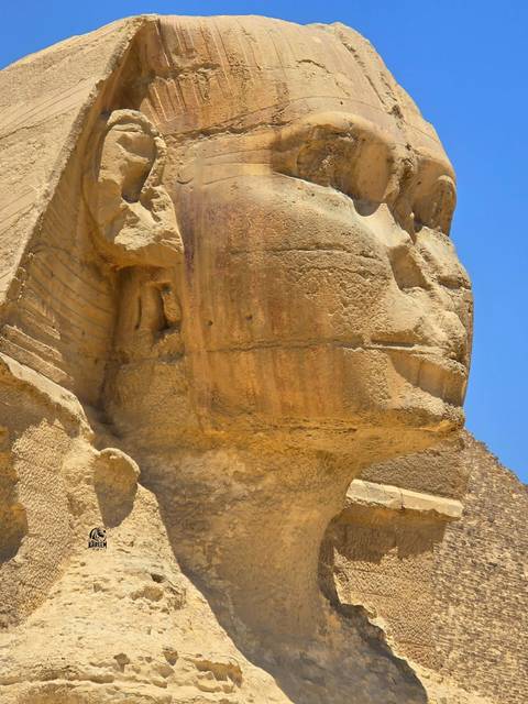 Close detail of the Great Sphinx of Giza's weathered stone profile against blue sky.