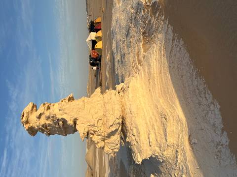 Eroded white limestone pinnacle in Egypt's White Desert near a campsite at golden hour.