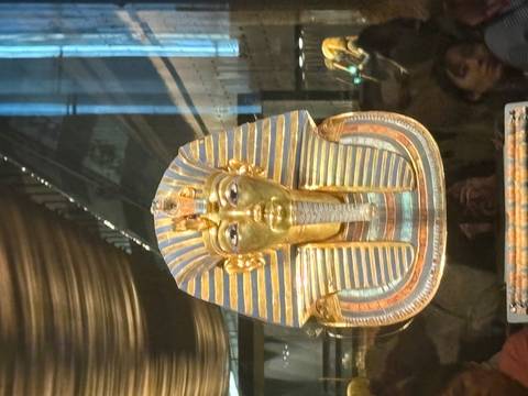 Golden funerary mask of Tutankhamun displayed behind glass in Cairo museum.