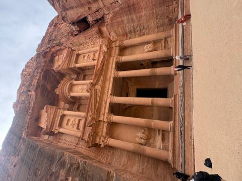The Treasury of Petra carved into rose-red sandstone cliffs with two visitors at its base.