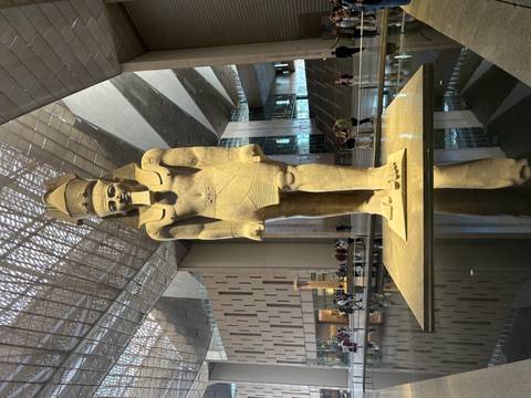 Massive statue of pharaoh within the Grand Egyptian Museum atrium reflected in a water feature.