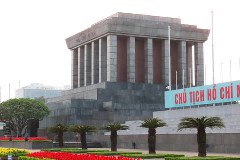 Grey-granite Ho Chi Minh Mausoleum with flagpoles and neat gardens in front.