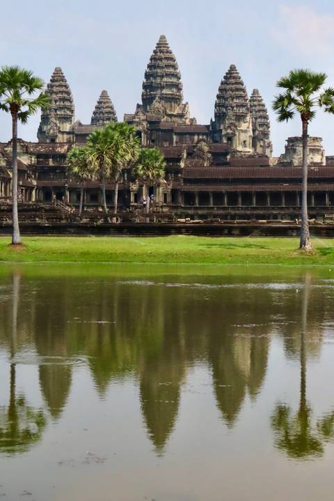 Stone temple complex reflected in a wide moat with green lawns in front.