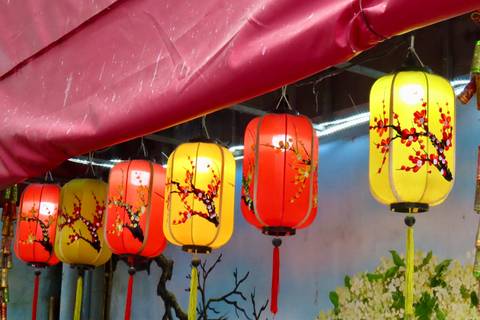 Row of colorful hanging lanterns with floral designs beneath a maroon canopy.