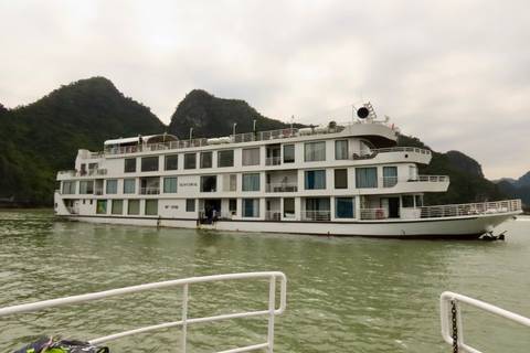 Modern white cruise ship gliding between forested limestone peaks on pale green water.