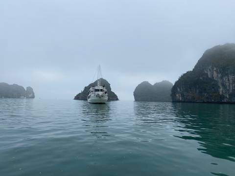 Single cruise boat anchored among mist-shrouded limestone islands on a calm bay.