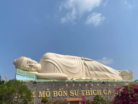 Giant reclining Buddha statue under blue sky at Mekong Delta temple complex.