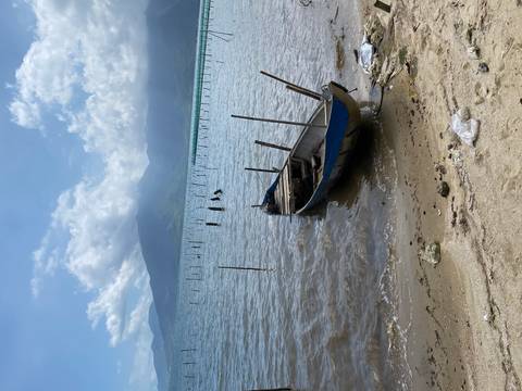 Weathered wooden boat rests on tranquil lagoon shore with misty mountains beyond.