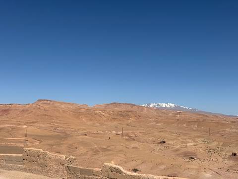 Vast arid Moroccan plateau with distant snow-capped mountain under a clear blue sky.