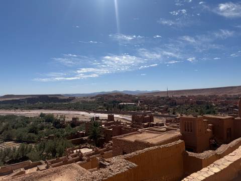 Panoramic view over the oasis valley and earthen kasbahs of Aït Benhaddou with mountains beyond.