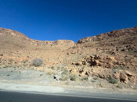 Rocky canyon wall and arid slopes under a cloudless deep-blue sky along a desert highway.