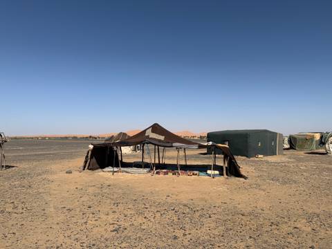 Traditional nomad tent camp on a flat stony plain with orange dunes visible in the distance.