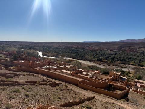 River meanders through a green oasis valley surrounded by reddish desert hills under bright sun.