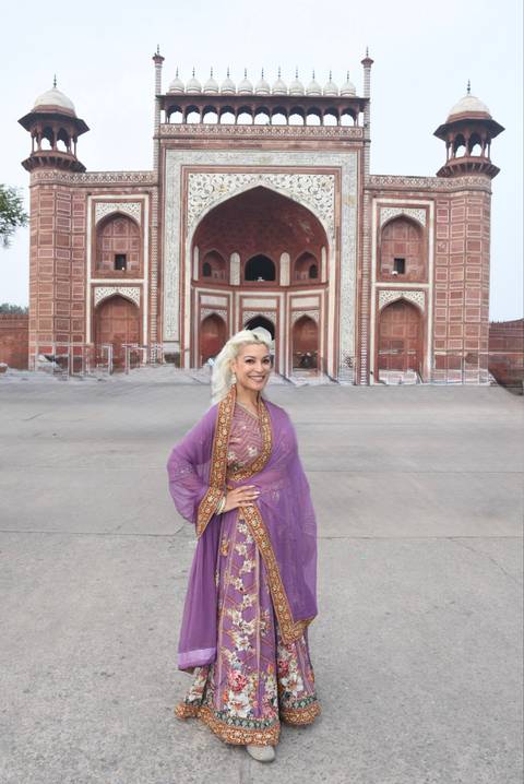 Smiling woman in purple traditional dress poses before ornate Mughal gateway