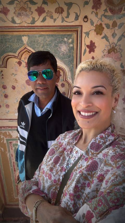 Two smiling travellers take a selfie in front of ornate frescoed wall