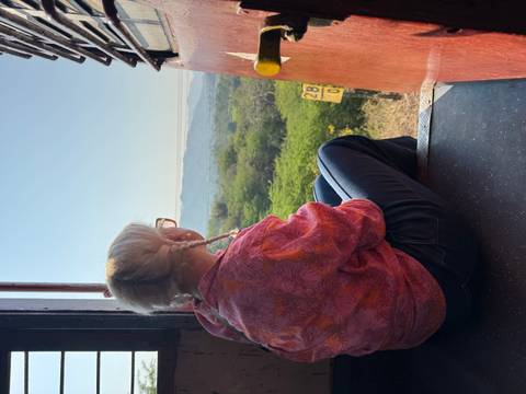 Traveller sitting in open train doorway looking over green valley landscape