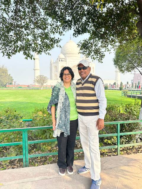 Smiling couple posing on lawns with Taj Mahal in background