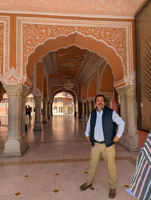Smiling man posing in an ornate orange-hued pillared hallway of an Indian palace