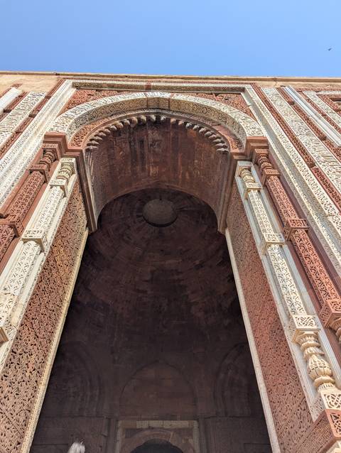Detailed view of carved red and white sandstone arch leading into a vast dome