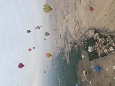 Dozens of colorful hot-air balloons floating above a patchwork of green fields and desert near the Nile.