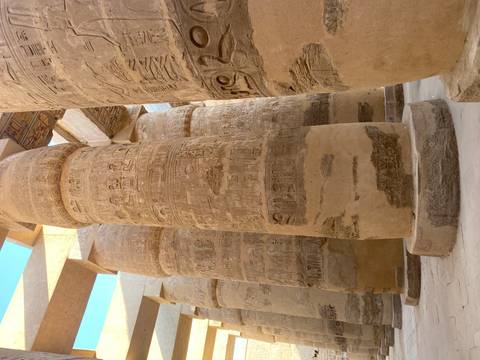 Gigantic sandstone columns covered in hieroglyphs inside the hypostyle hall of Karnak Temple.
