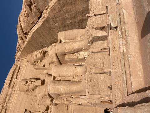Monumental seated statues at Abu Simbel carved directly into a sandstone cliff bathed in warm sunlight.